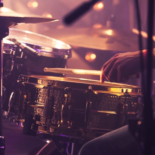 Vintage toned live music background, drummer plays with drumsticks on rock drum set. Closeup photo with soft selective focus