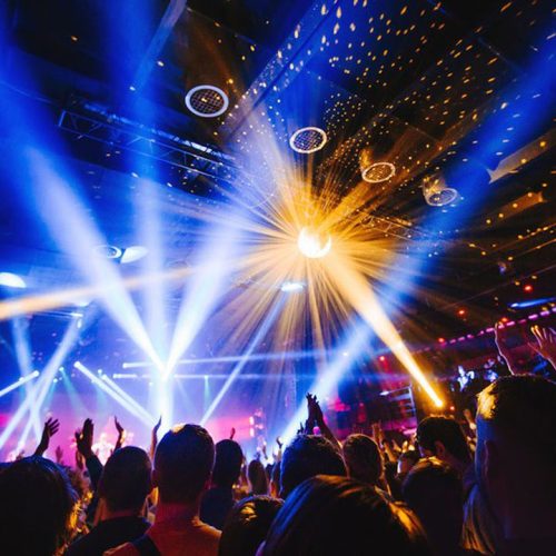 silhouette of concert crowd in front of bright stage lights. Dark background, smoke, concert  spotlights, disco ball